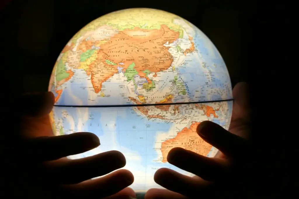Photo of glowing globe showing the countries located in Asia. The globe is being cradled in the hands of a person.