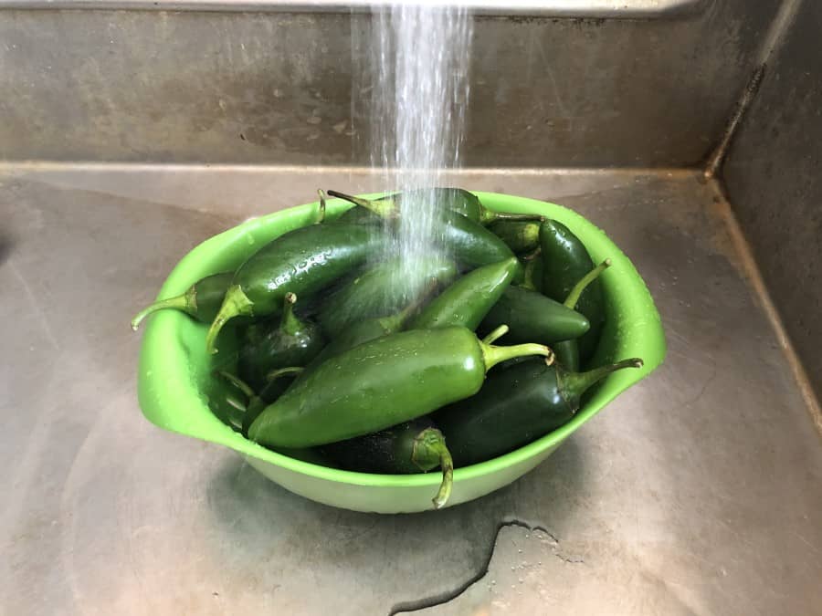 Photo of a green bowl full of green Jalapeno peppers being rinsed off with water.