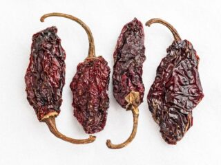 Photo for four deep brown dried chipotle peppers. The peppers are pointing upward and downwards in an alternating fashion
