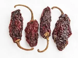 Photo for four deep brown dried chipotle peppers. The peppers are pointing upward and downwards in an alternating fashion