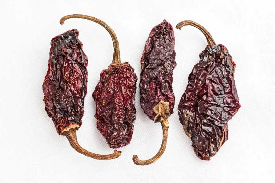 Photo for four deep brown dried chipotle peppers. The peppers are pointing upward and downwards in an alternating fashin