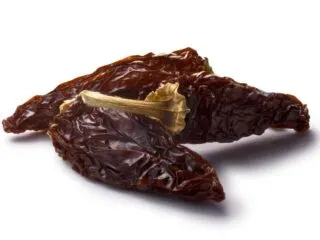 Photo of three dried deep brown chipotles laying down on a white background. One of the chipotle peppers is propped up onto the pepper closest to the camera.