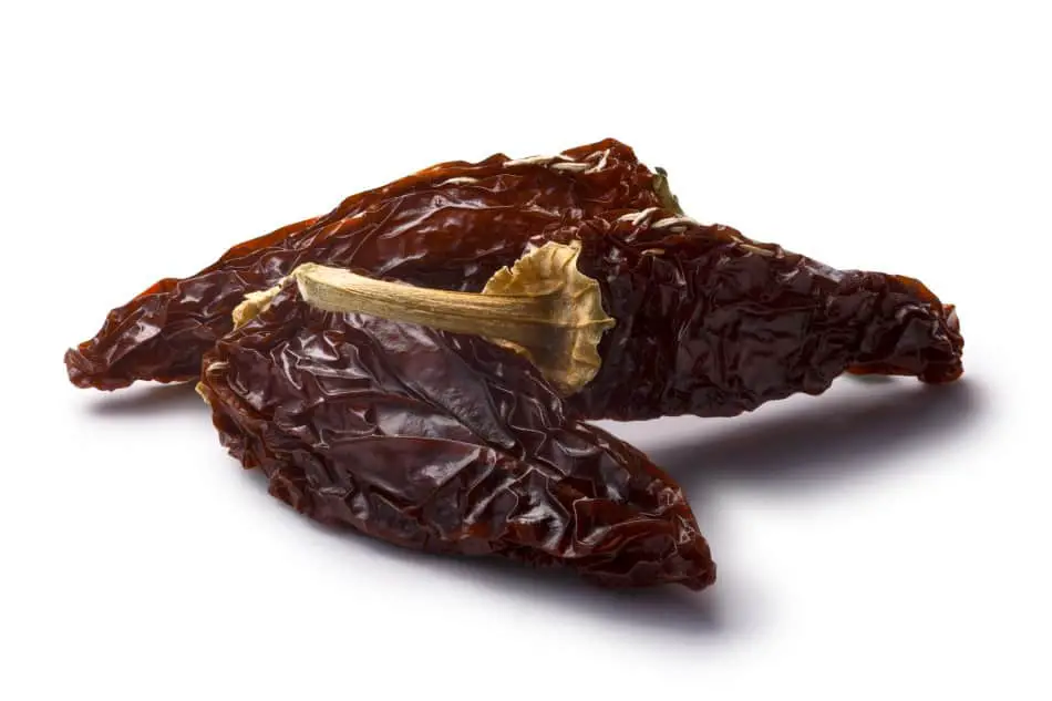 Photo of three dried deep brown chipotles laying down on a white background. One of the chipotle peppers is propped up onto the pepper closest to the camera.