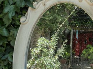 Photo of ornamental garden mirror with reflection of gravel pathway and some plants