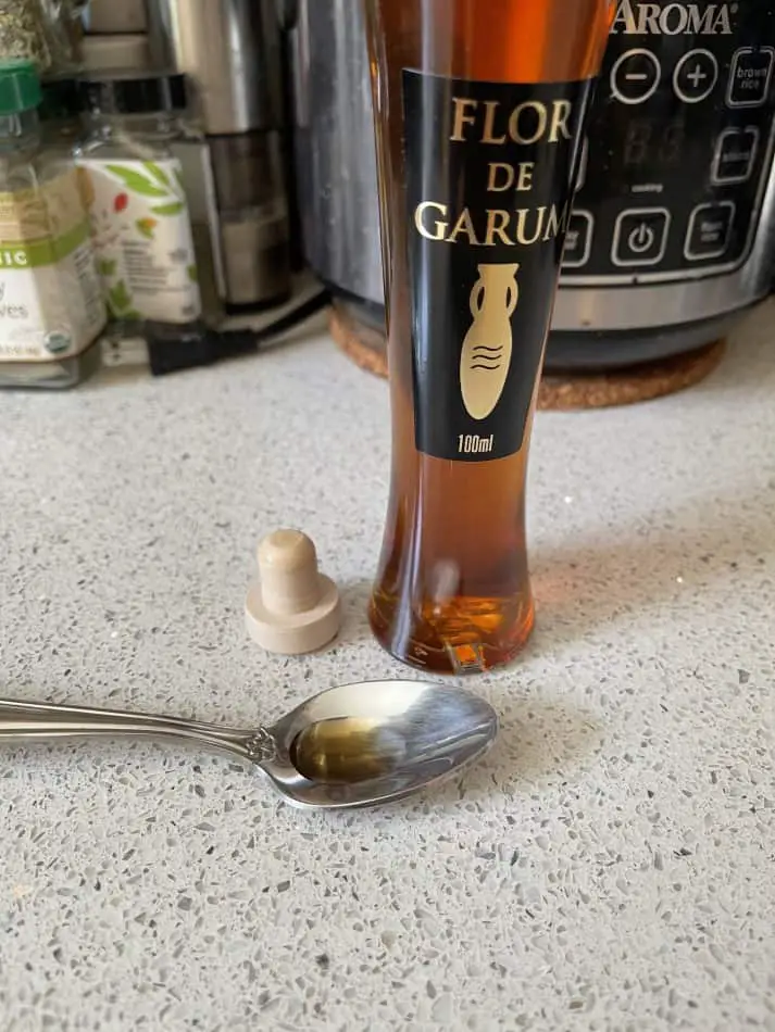 Photo of Garum fish sauce, a reddish brown liquid, in a thin bottle and on a stainless steel spoon