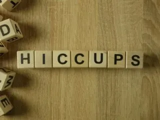 Photo of wooden scrabble pieces on a wood desk that spell Hiccups