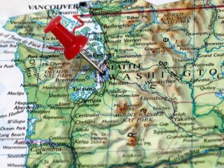 Photo of the Washington state map with a red thumb tack pinned to Seattle at angle