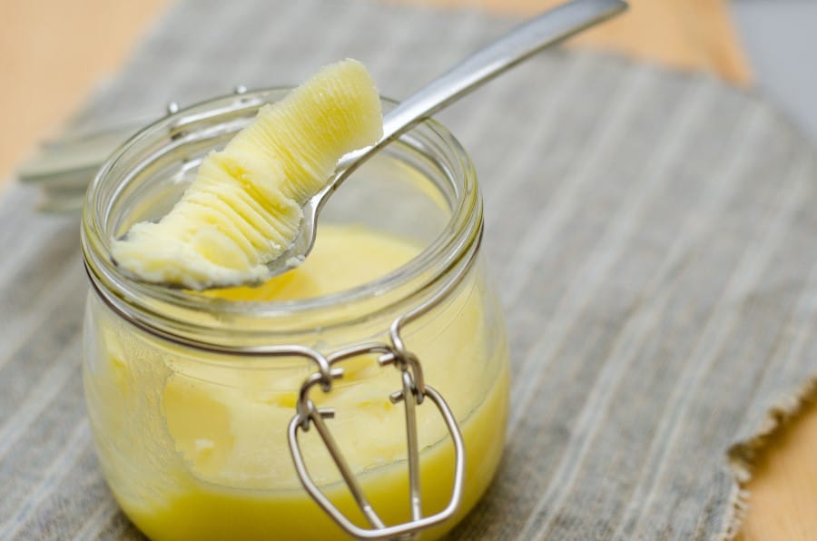 Photo of cold ghee in a short glass jar. Some of the ghee is being removed from the container with a fork