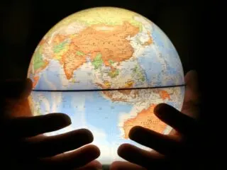 Photo of glowing globe showing the countries located in Asia. The globe is being cradled in the hands of a person.