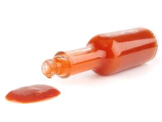 Photo of a tipped over bottle of hot sauce on a white backdrop. The hot sauce has spilt out of the open end of the bottle.