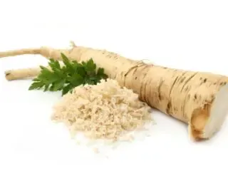 Photo of horseradish root next to a sprig of green leaves and a ground mound of horseradish on a white backdrop