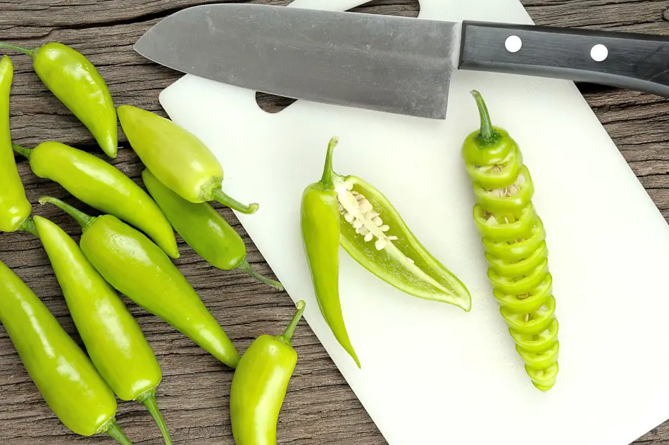 Photo of many banana peppers to the left of a plastic chop board with a sliced up banana pepper on top of it