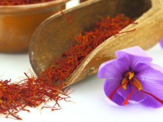 Photo of saffron pouring out of a wood spoon with a saffron flower to the lower right