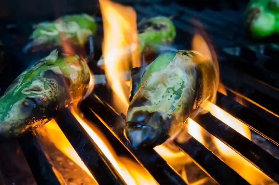 Photo of two green chili peppers being fire roasted on a grilll