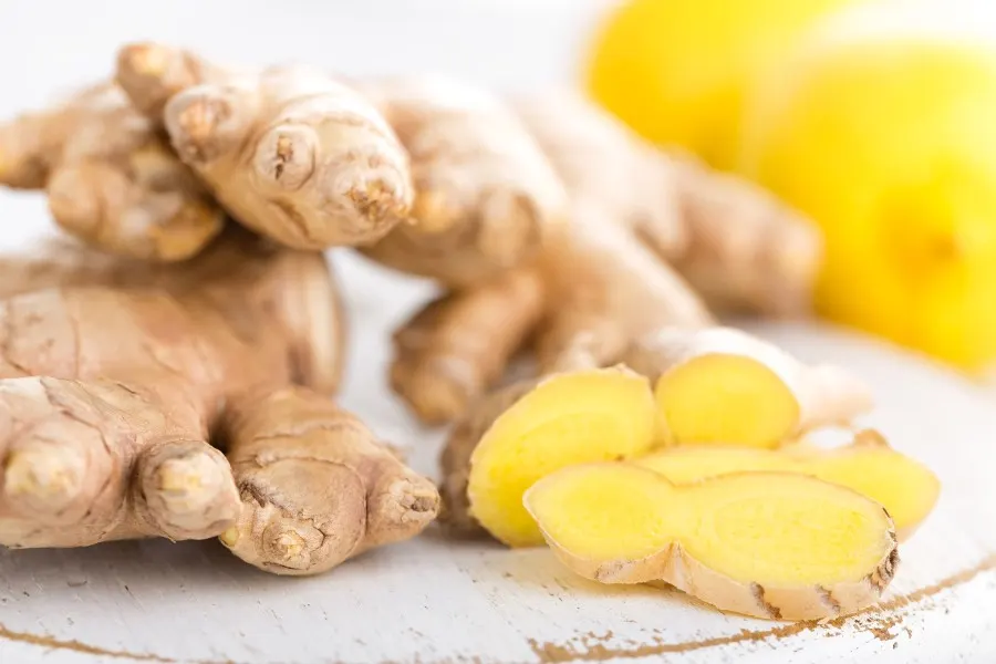 Photo of ginger sliced open on a counter with two lemons in the background