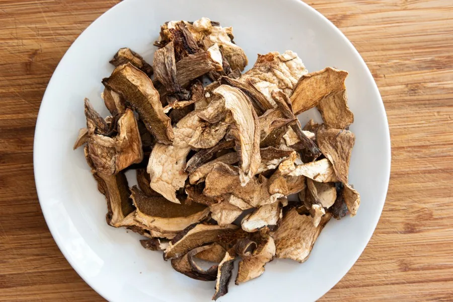 Dehydrated mushrooms piled up in a white bowl sitting on a wooden background