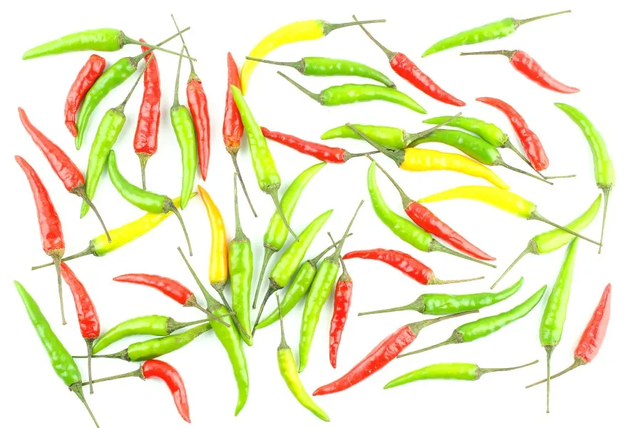 Photo of thin long yellow, green, and red thai chili peppers scattered against a white background