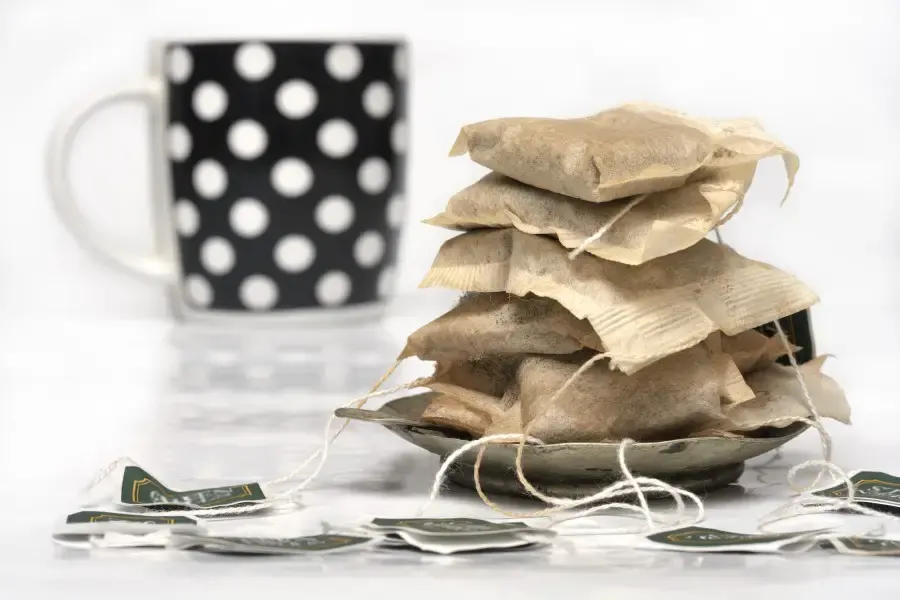 Photo of used teabags stacked on each other with a mug in the background