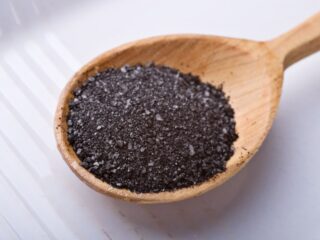 Photo of black salt sitting in a big wooden spoon