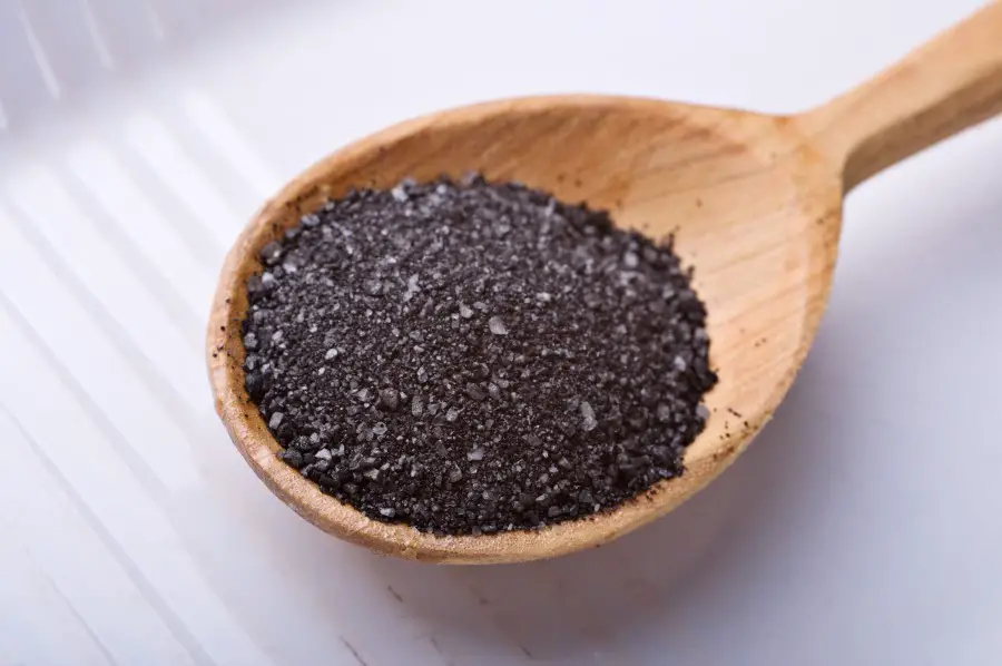 Photo of black salt sitting in a big wooden spoon