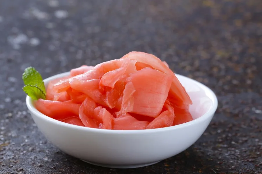 Photo of pink pickled ginger placed in a small white bowl with a single green mint leaf