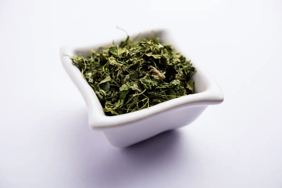 Dried Kasoori methi in a small square shaped white vessel