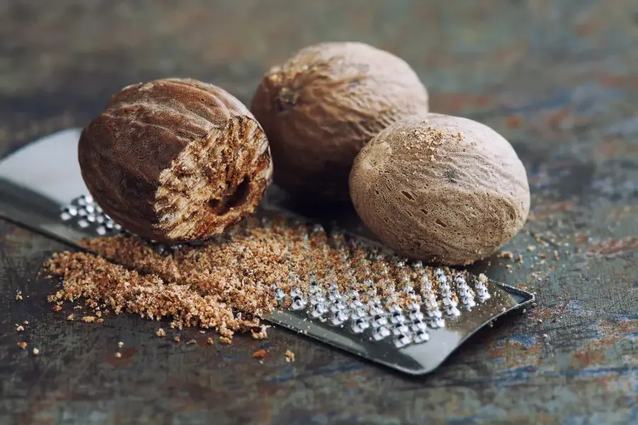 Photo of a partially ground whole nut meg sitting on top of a grinder with two other whole nutmegs to its left