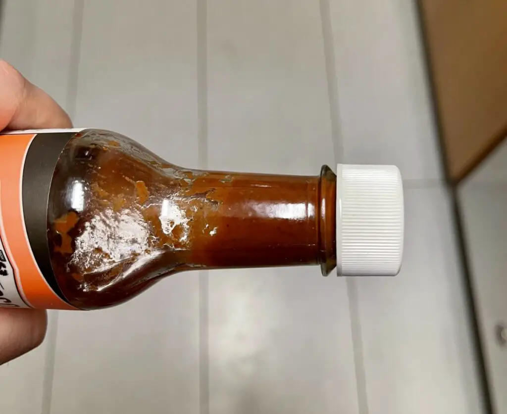 Side shot of a hot sauce bottle neck with hot sauce that has turned brown